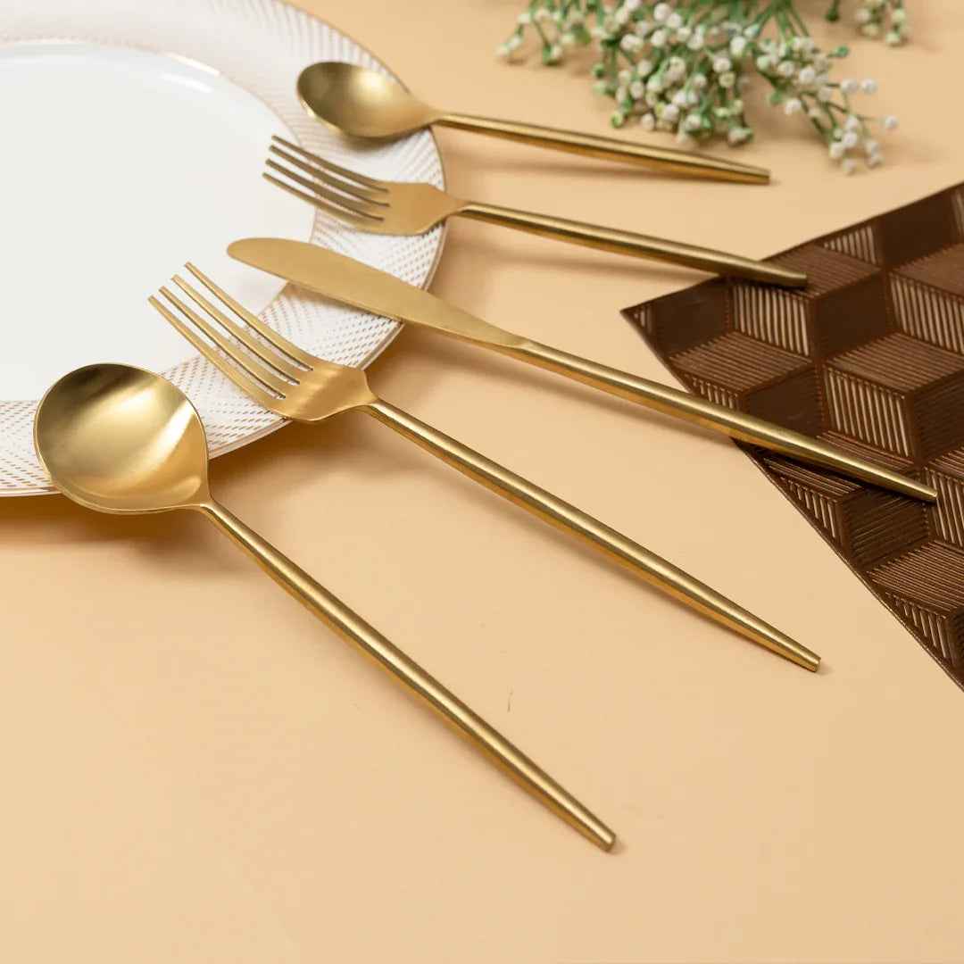 Gold cutlery set on a beige surface with a white plate and decorative elements.