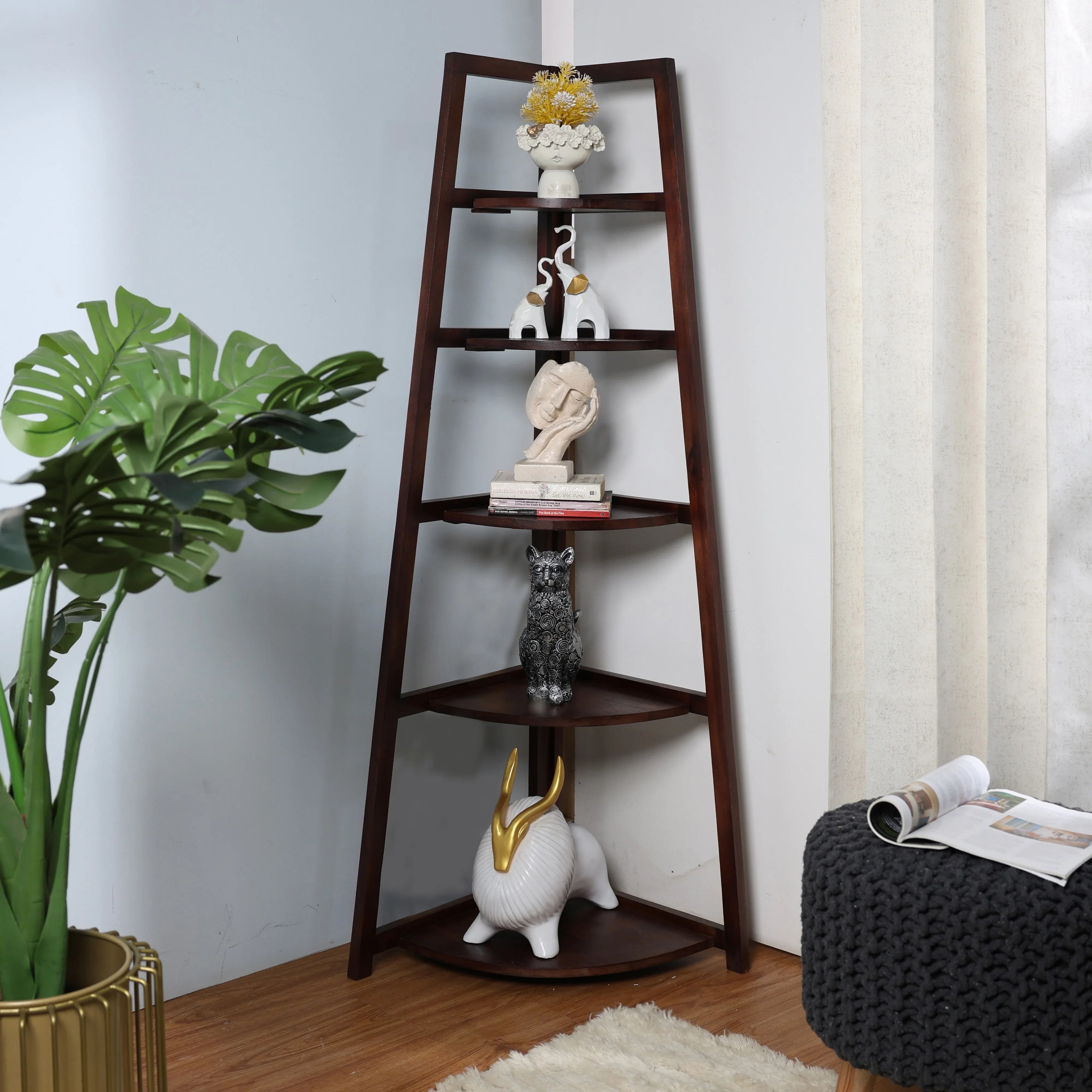 A wooden 5 tier corner ladder shelf with various decorative items placed on each tier, positioned in a room corner beside a window and a potted plant.