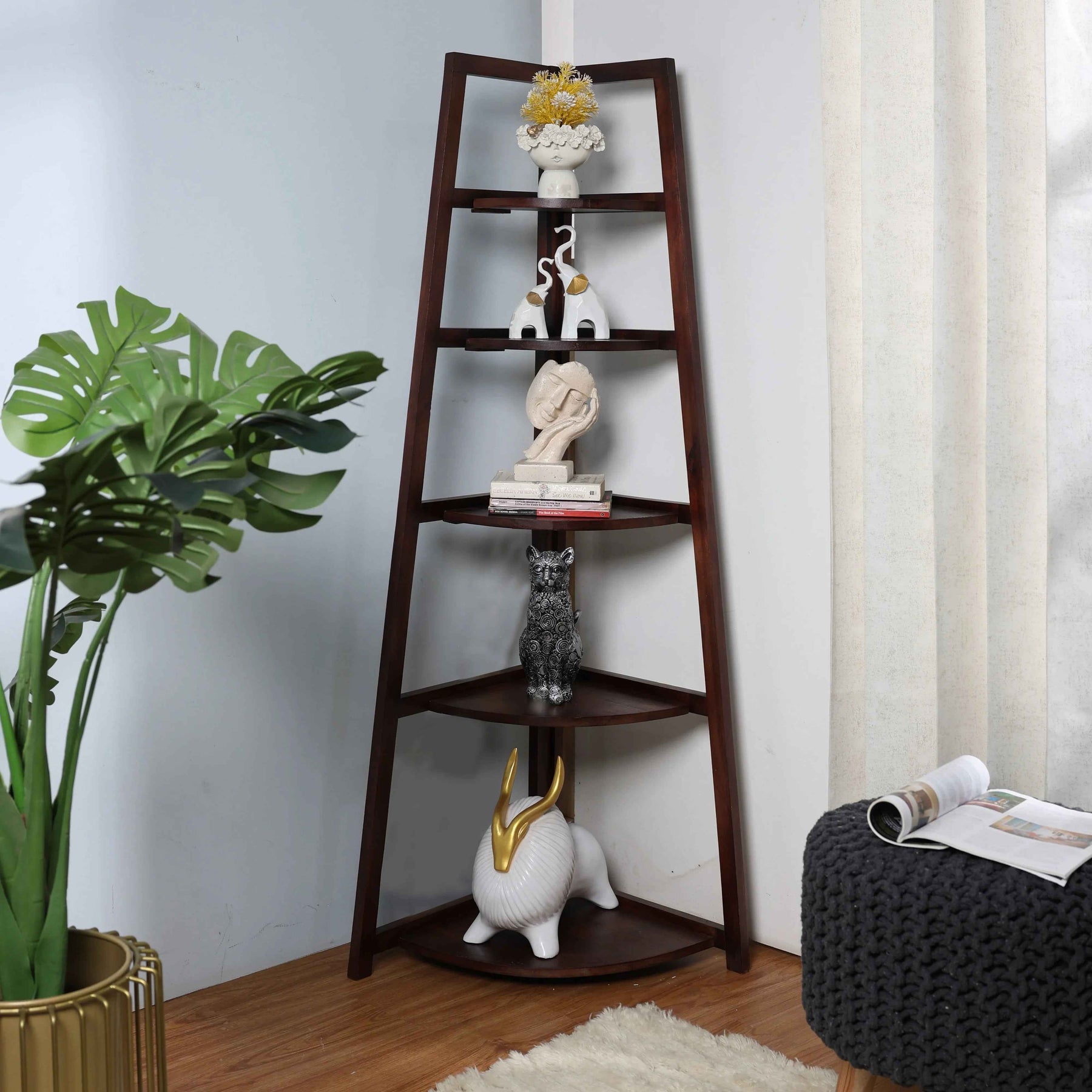 A wooden 5 tier corner ladder shelf with various decorative items placed on each tier, positioned in a room corner beside a window and a potted plant.