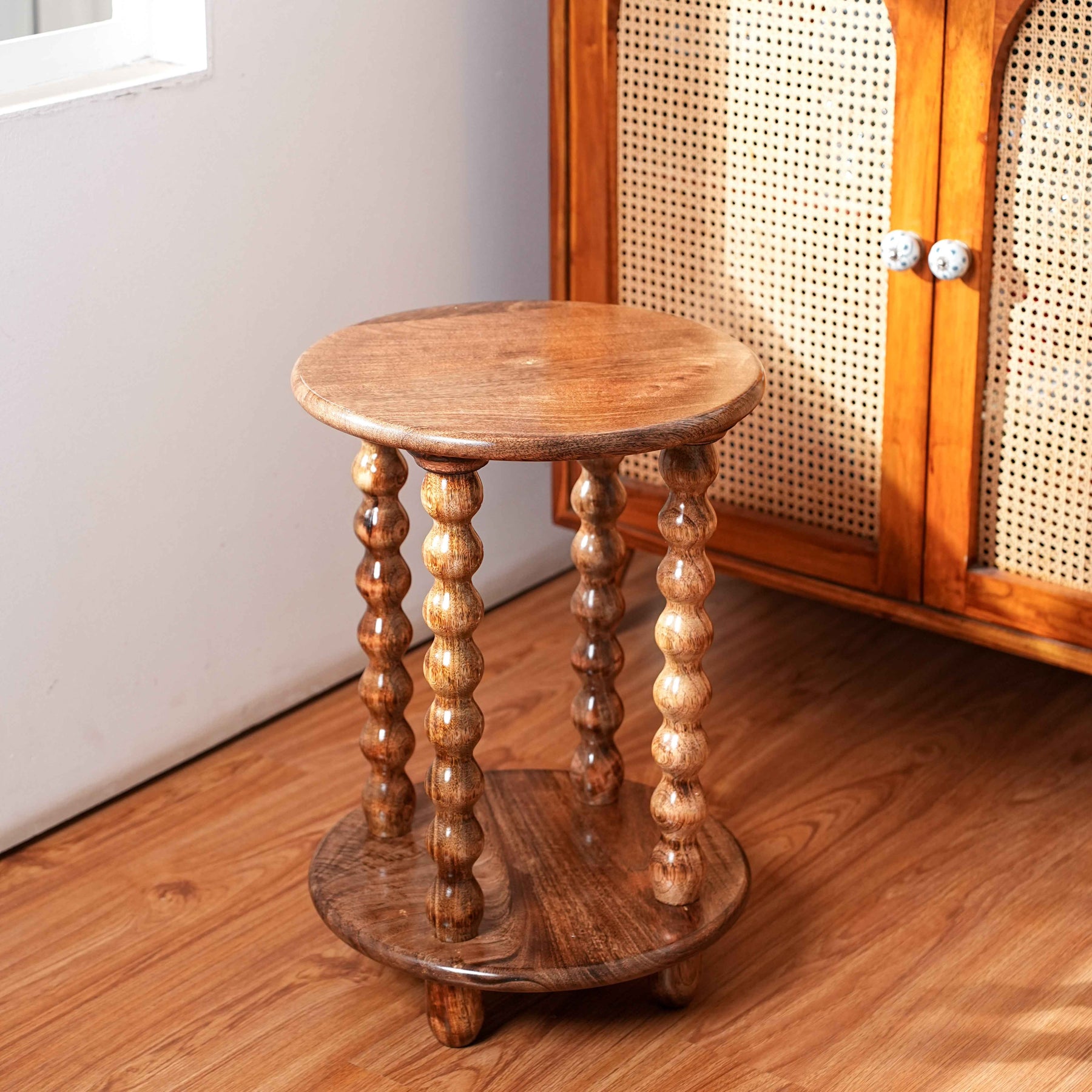Wooden side table with spiral legs on a wooden floor next to a cabinet.