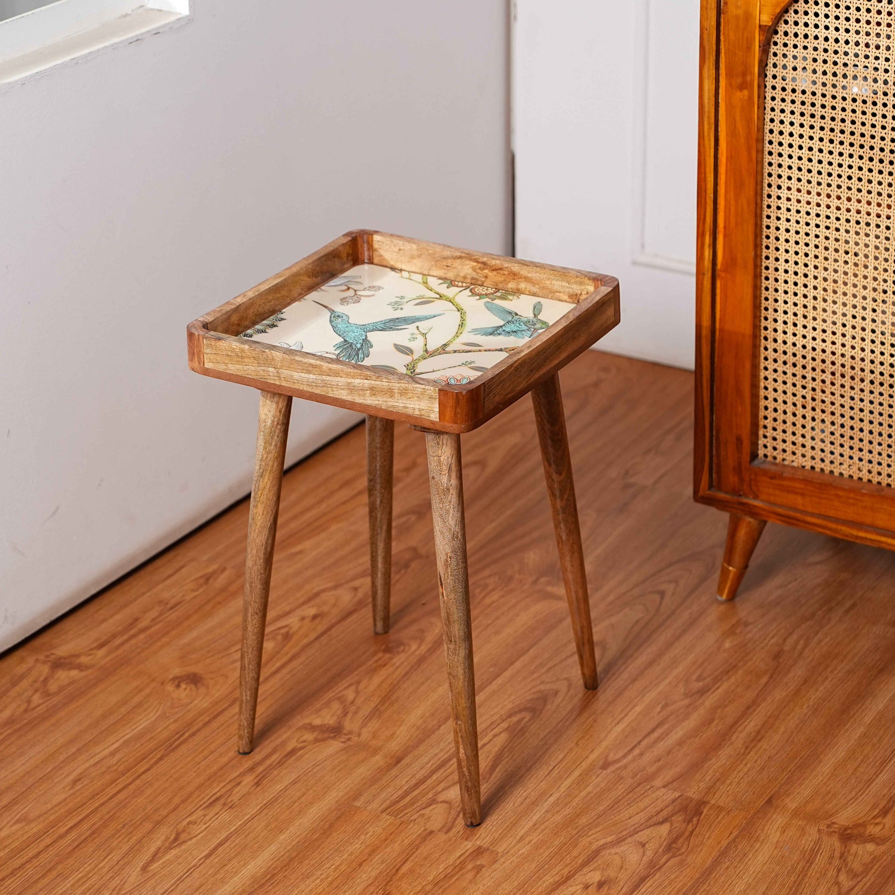 Wooden side table with a decorative cushion on a wooden floor.