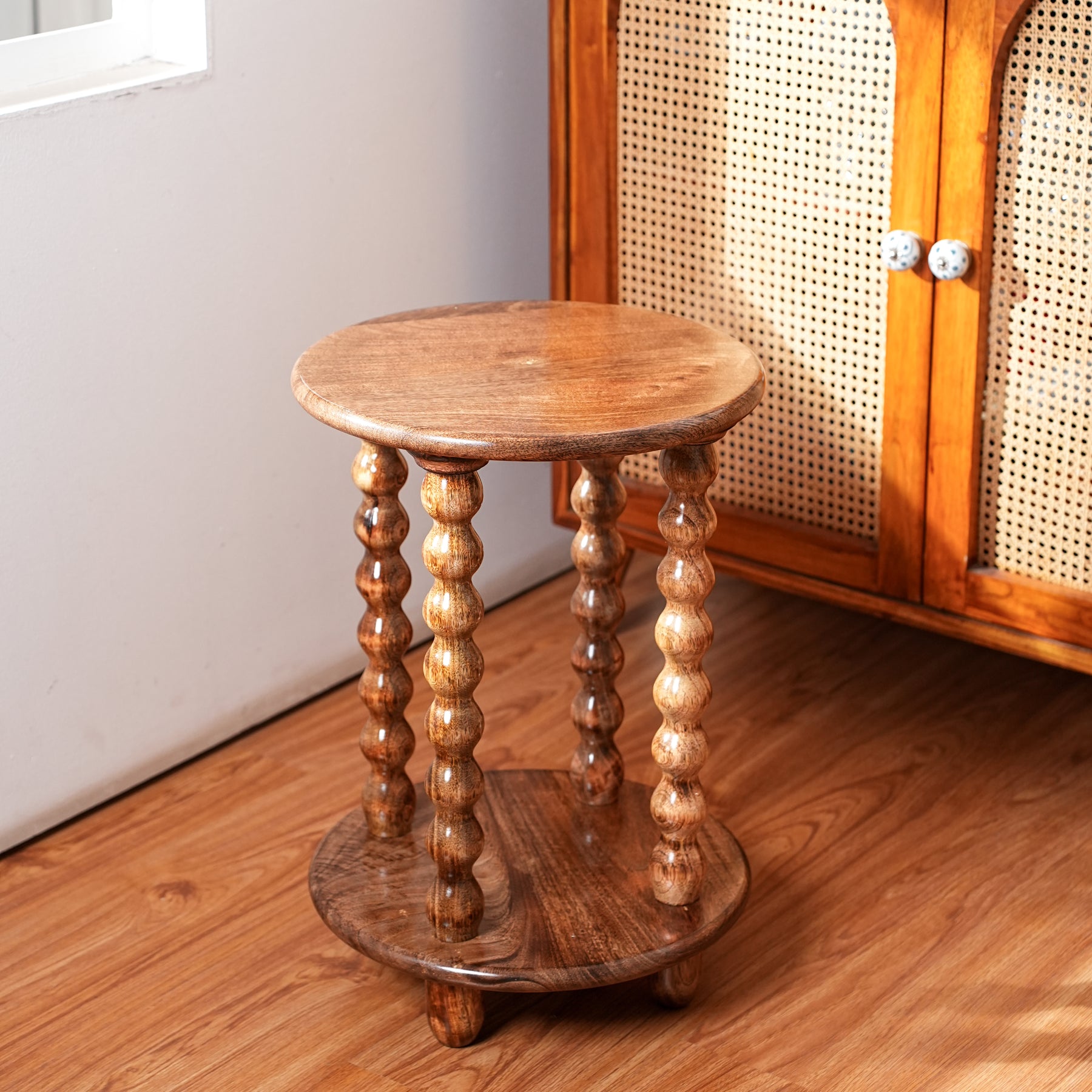 Wooden side table with spiral legs on a wooden floor next to a cabinet.
