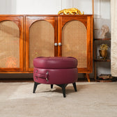 Maroon ottoman with suitcase design in front of a wooden cabinet.