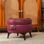 Round purple ottoman with black legs in front of a wooden cabinet.