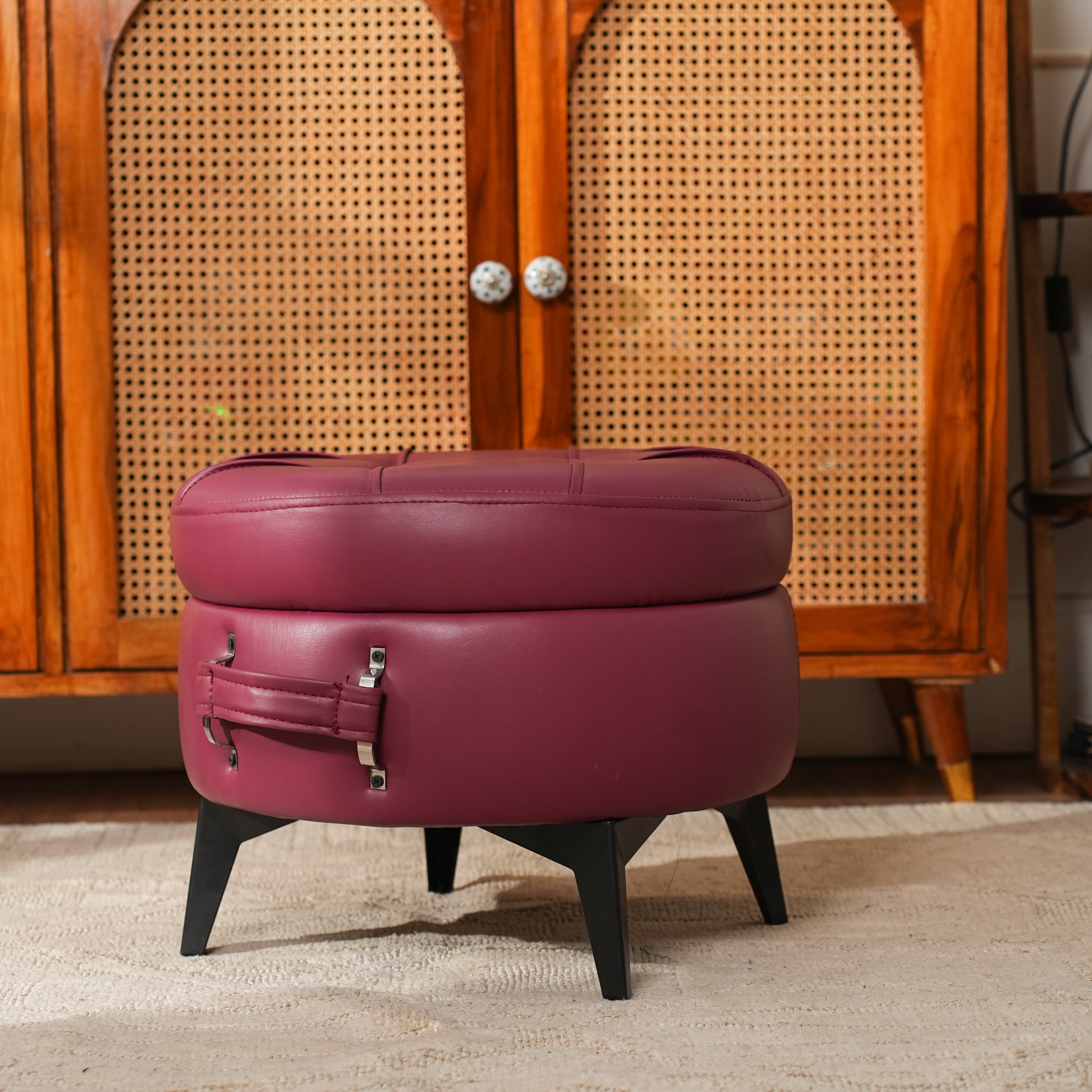 Round purple ottoman with black legs in front of a wooden cabinet.